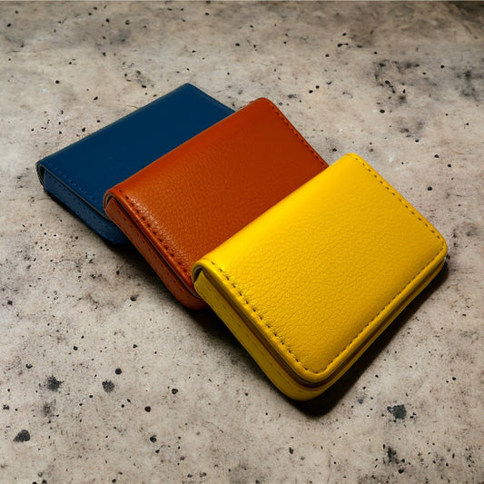 Bündel fröhlicher Farben: Unsere Kartenhalter in Blau, Gelb, Orange und Pink bilden einen farbenfrohen Kontrast zum schlichten Betonhintergrund – ein stilvolles, praktisches Ensemble für Karten und Dokumente.