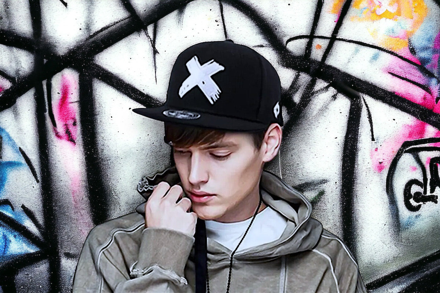 Vorschaubild einer Snapback Cap, präsentiert von einem attraktiven jungen Mann, mit einer farbenfrohen Graffiti-Wand im Hintergrund, entstanden in Berlin.
